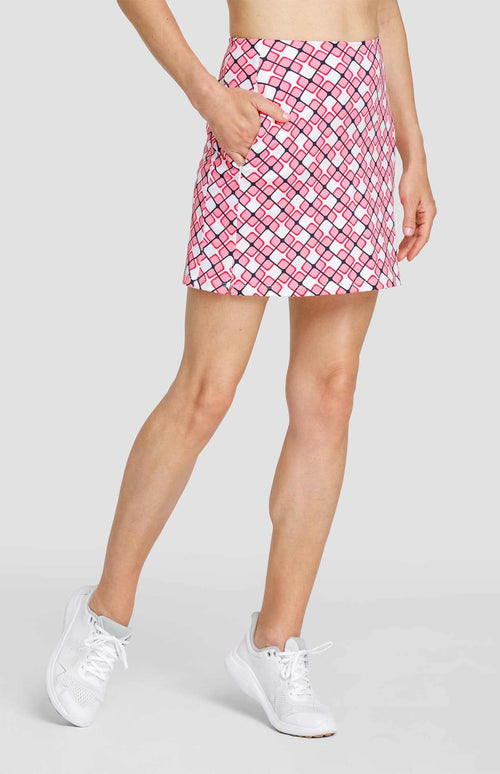 Bottom half of a woman wearing a pull-on skort with a light pink and white geometric print with dark navy blue lines. Her hand is in the front pocket.