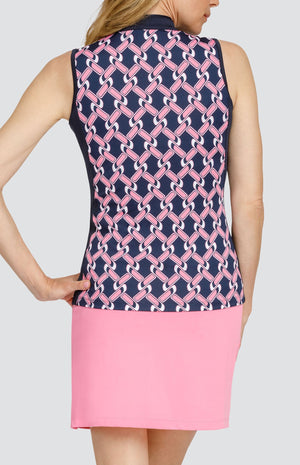 Back view of a woman wearing a sleeveless golf top. The print is a light pink and white chain geometric pattern on a dark navy blue background. There are dark navy blue side inserts. She is also wearing a light pink golf skort.