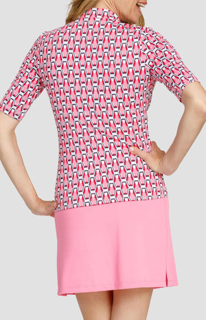 Back view of a woman wearing a mid-length sleeve golf top. The print is a geometric pattern of 6-sided gemstones in a light pink color on a white background. She is also wearing a light pink golf skort.