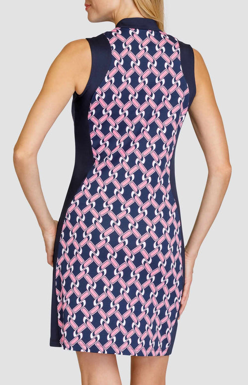 Back view of a woman wearing a sleeveless golf dress. The print is a light pink and white chain geometric pattern on a dark navy blue background. There are dark navy blue side inserts from the shoulder to the hem. 