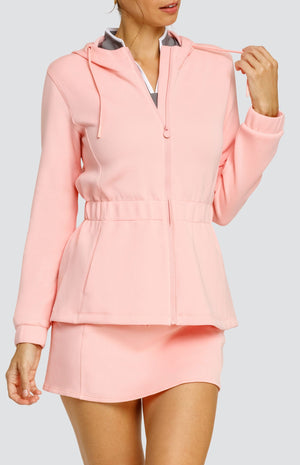 Model wearing a light pink hooded jacket with a cinched waist and drawstring hood. Paired with a matching skort with drawstring waistband, and a gray top with white accents.